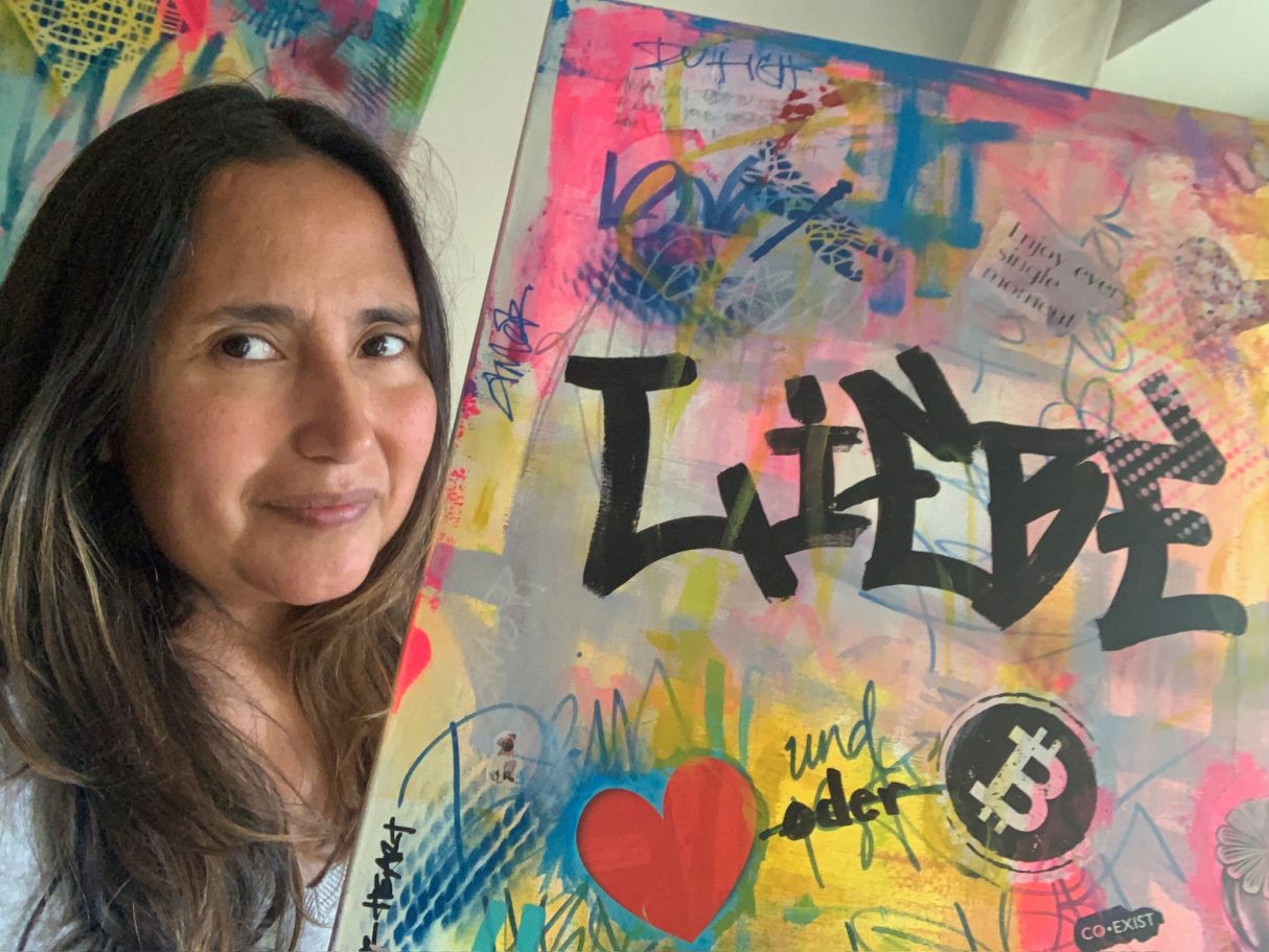 Artist standing with a colorful urban art painting featuring the word “Liebe”